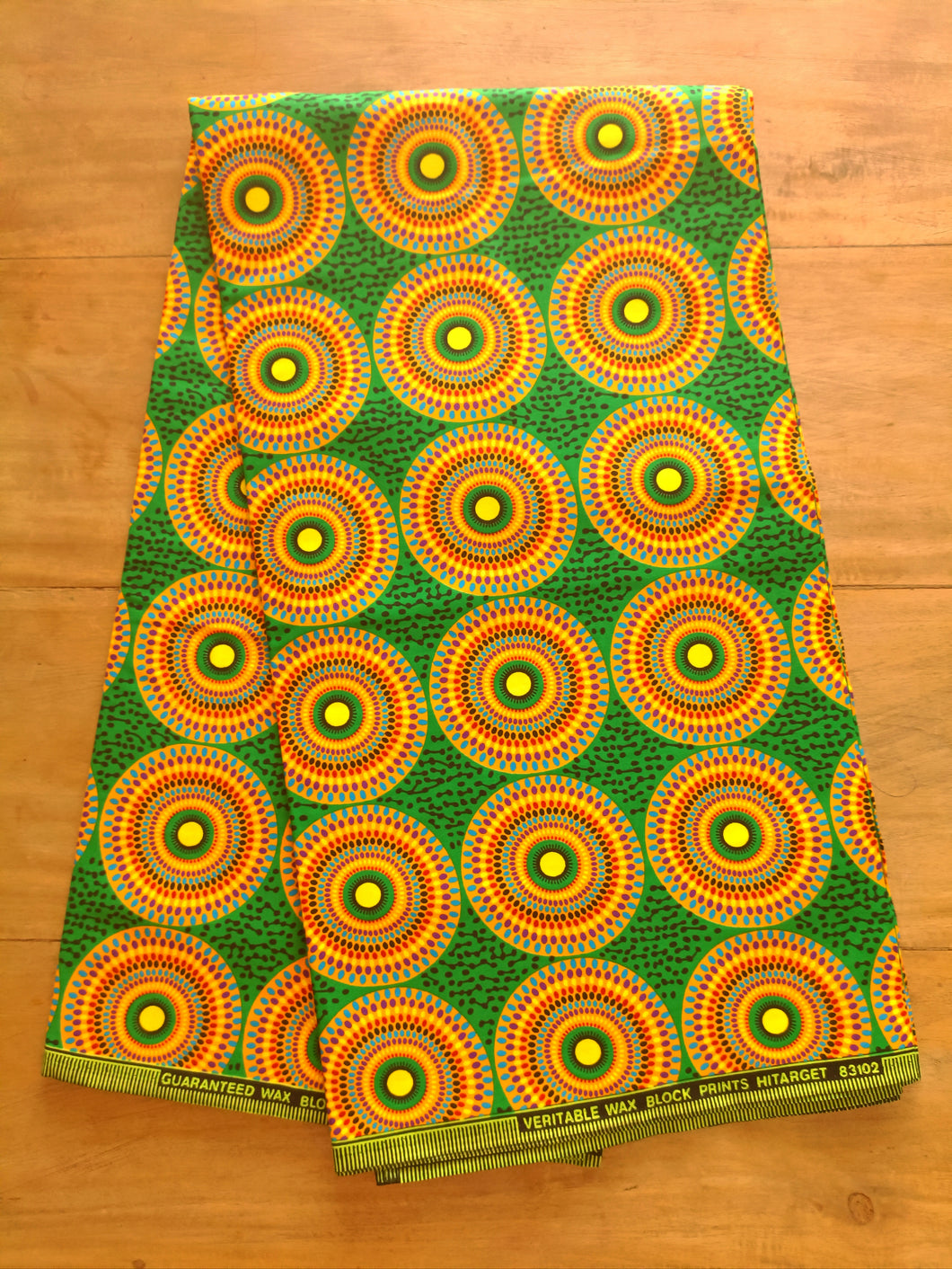Tissu wax - petits disques jaunes et multicolores sur fond vert - par 50 centimètres